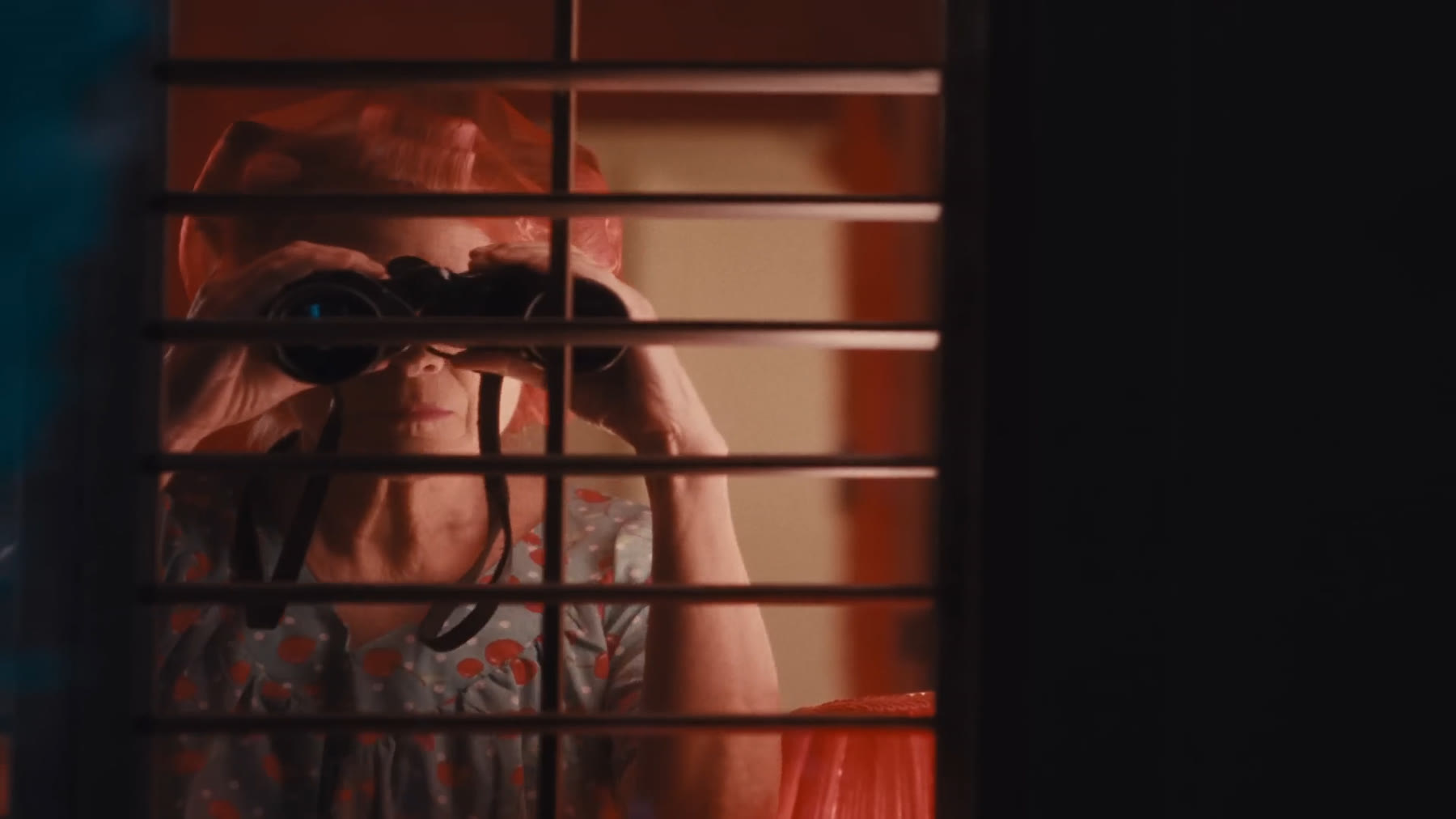 An older woman peering through her blinds